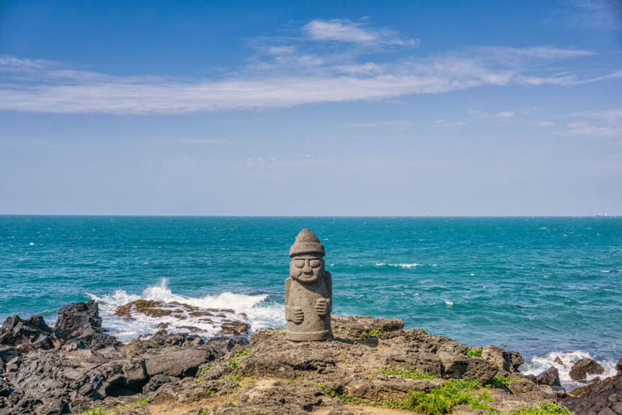 Basalt Dolhareubang statue on Jeju Island beach, symbolizing local tradition and culture in a scenic coastal setting