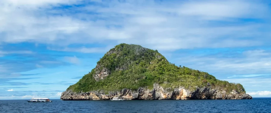 Malapascua Gato Island domed rock island with boats, cliffs and vegetation, Philippines seascape.
