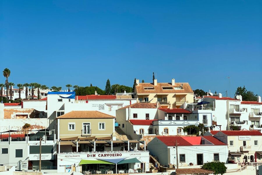 Charming Quarteira coastal town with colorful architecture and Restaurante Don Carvoeiro amid palm trees.
