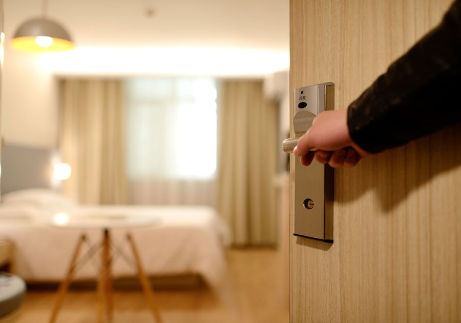 Hand opening hotel room door with electronic lock and modern handle.