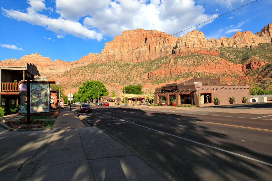 Downtown Springdale, Utah, showcasing vibrant storefronts and the majestic backdrop of red rock cliffs under a clear sky.
