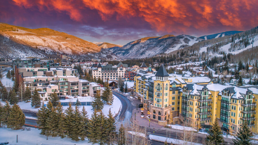 Aerial view of Vail, Colorado at sunset, showcasing the downtown skyline with vibrant colors illuminating the buildings