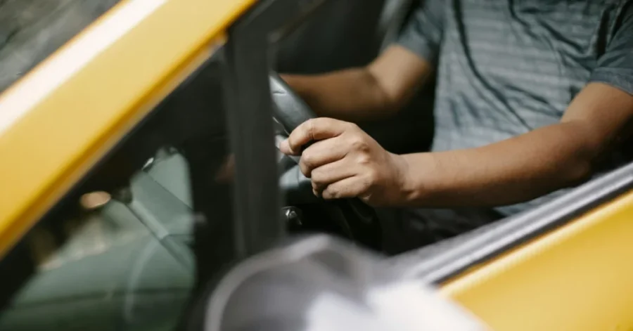 Taxi driver hands on steering wheel in yellow car.