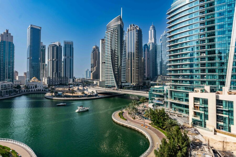 Dubai Marina skyline with modern skyscrapers, serene waterway, and lush greenery on a sunny day.