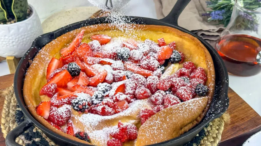 Dutch baby pancake in cast iron skillet with fresh berries and powdered sugar for brunch.