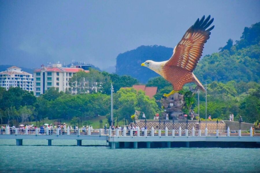 Majestic eagle statue on coastal pier with lush greenery and visitors.