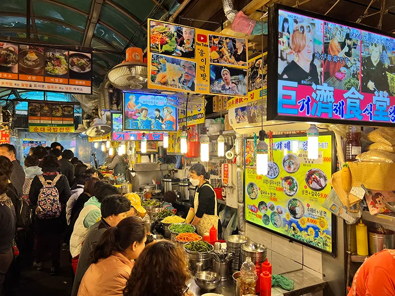 Bustling East Asian street food market with diverse dishes, vibrant signs, and lively atmosphere.