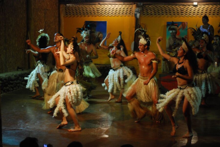 Traditional Rapa Nui dancers performing on Easter Island stage in vibrant feathered costumes.