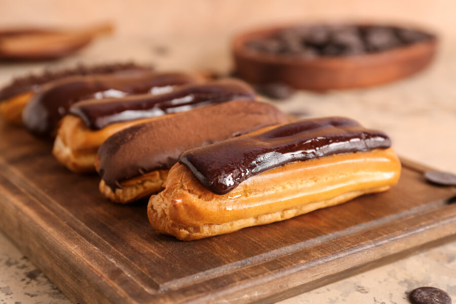 Closeup view of a wooden board featuring an assortment of delectable chocolate eclairs on a table