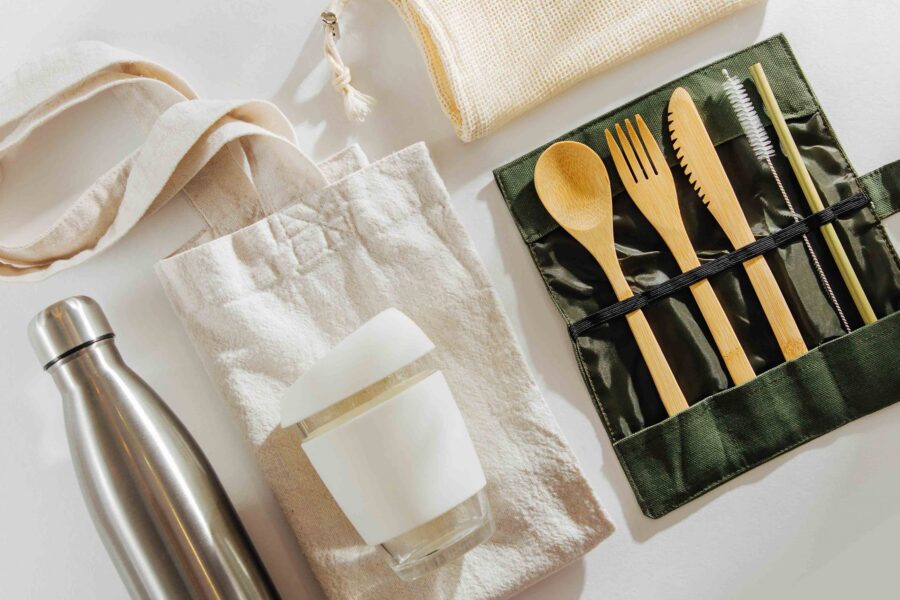 Eco-friendly travel essentials: reusable bottle, glass container, utensils, cloth bag, and mesh pouch.
