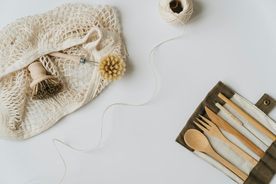 Eco-friendly kitchen tools on white background: net bag, wooden utensils, natural fiber brushes.