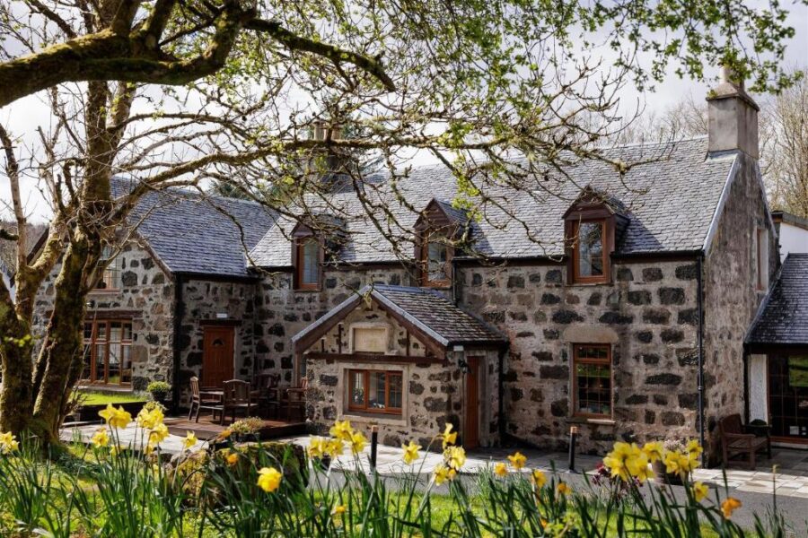 Edinbane Lodge in the UK, surrounded by vibrant daffodils and lush trees, creating a picturesque landscape.
