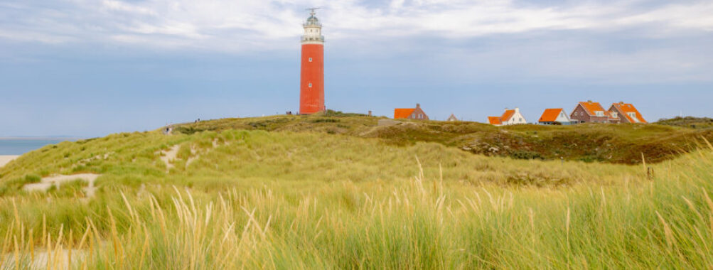 Red Eierland Lighthouse on Texel island, surrounded by sand dunes and marram grass under a clear blue sky in North Holland.