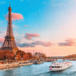 The iconic Eiffel Tower bathed in sunset light, alongside the Seine River, featuring cruise ships in the picturesque scene