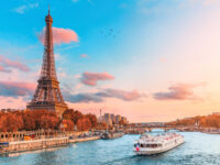 The iconic Eiffel Tower bathed in sunset light, alongside the Seine River, featuring cruise ships in the picturesque scene