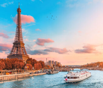 The iconic Eiffel Tower bathed in sunset light, alongside the Seine River, featuring cruise ships in the picturesque scene