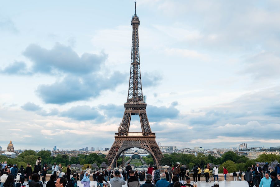 Eiffel Tower in Paris under a vibrant sky with clouds and crowds enjoying the scene.