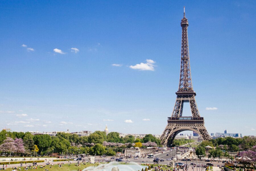 Eiffel Tower on a sunny Paris day with greenery and visitors enjoying the scene.