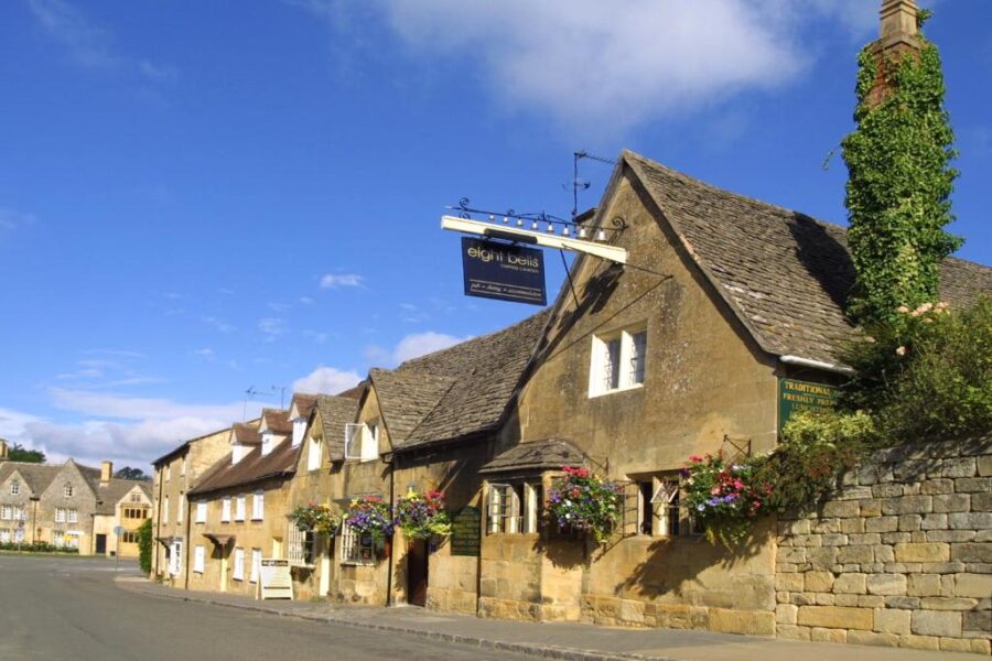 Cobblestone street lined with historic stone buildings, featuring the Eight Bells Inn in the UK.