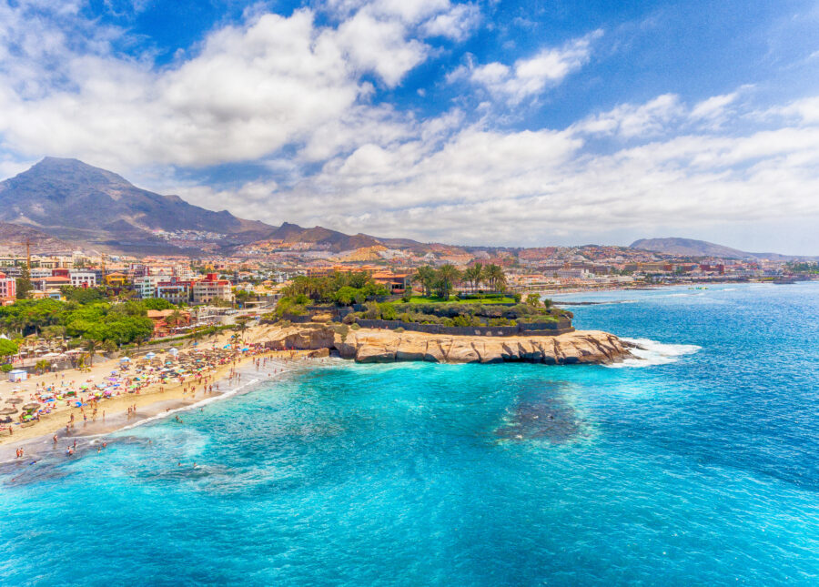 Aerial view of El Duque Beach in Tenerife, Spain, showcasing golden sands and clear blue waters surrounded by lush greenery.