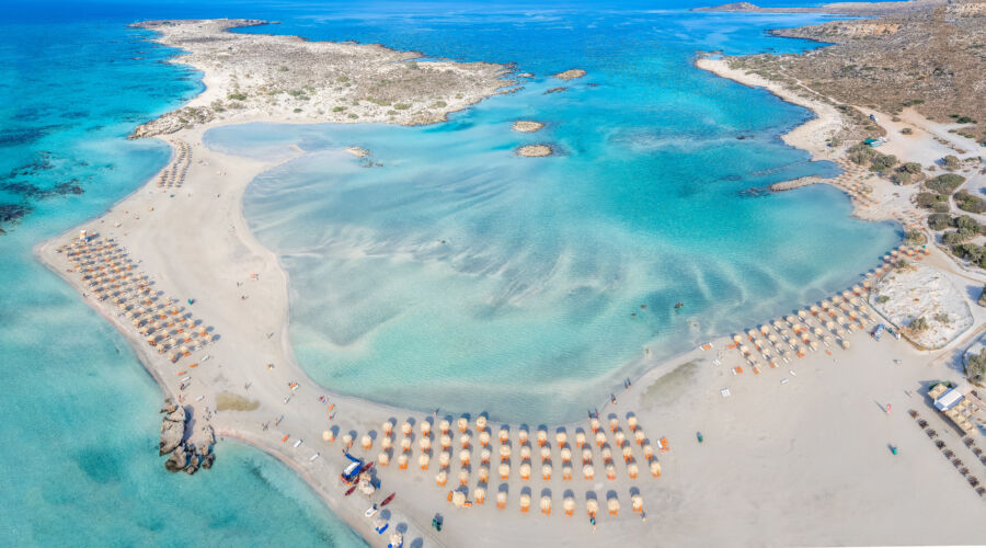 Aerial view of Elafonissi beach in Crete, showcasing its pink sands and turquoise waters surrounded by lush greenery.
