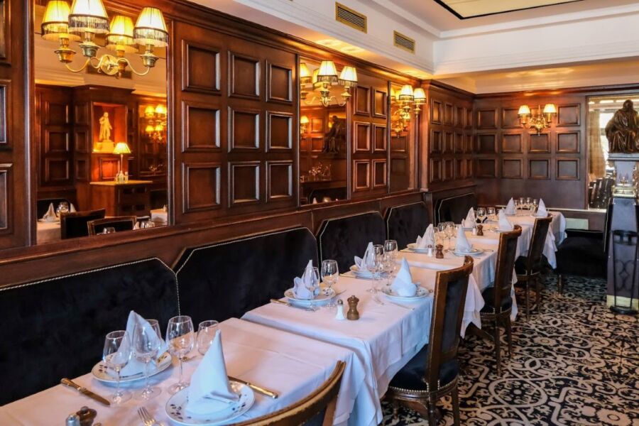 Elegant restaurant interior with wooden paneling, soft lighting, plush chairs, and immaculate table settings.