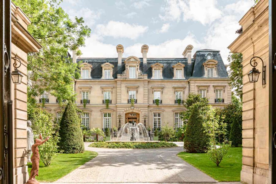 Elegant French mansion with a landscaped garden, fountain, classical sculpture, and dormer windows.