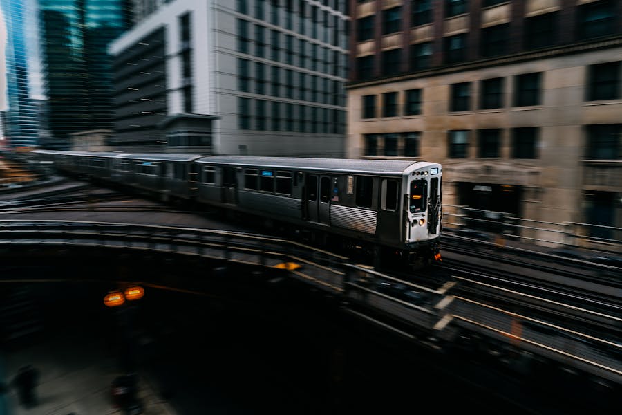 Silver elevated train curving through an urban canyon of city buildings.
