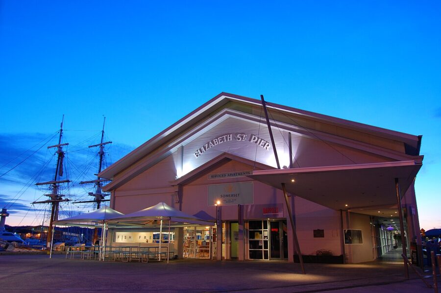 Elizabeth Street Pier waterfront restaurant and marina at dusk with umbrellas and sailboat masts.
