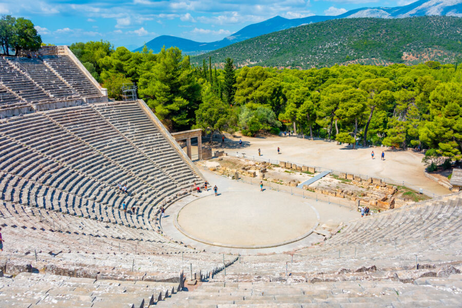 Ancient Epidaurus Theatre, showcasing its well-preserved stone seating and scenic backdrop of lush hills and trees.