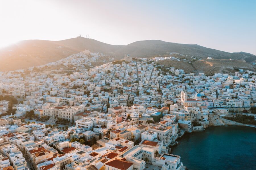 Aerial view of Vaporia district in Ermoupoli, showcasing colorful homes by the turquoise coast of Syros island, Greece.