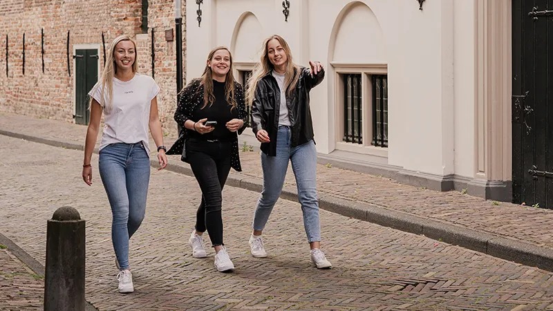 Three young women stroll down a cobblestone street during the Escape Tour in The Hague.
