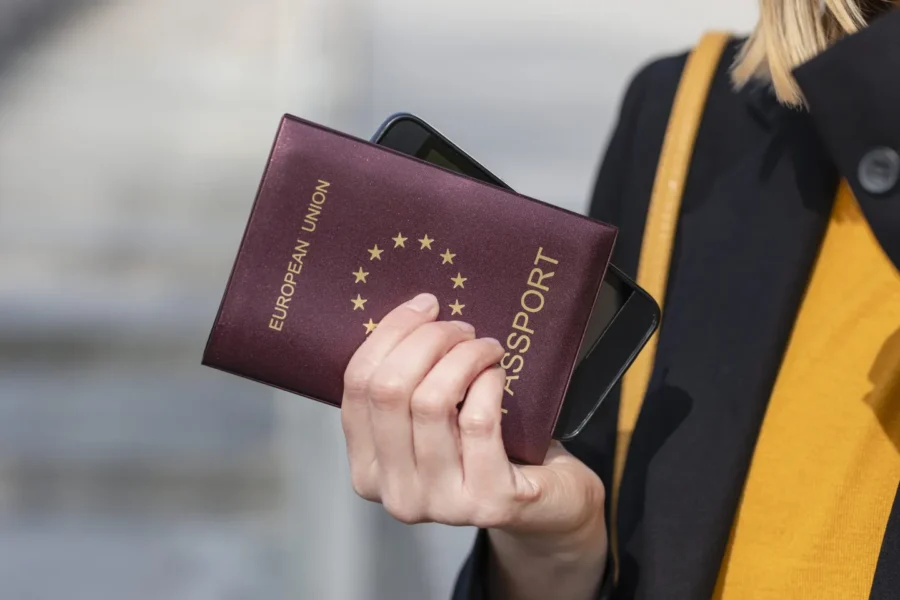 Traveler holding European Union passport and smartphone, close-up travel document photo outdoors.