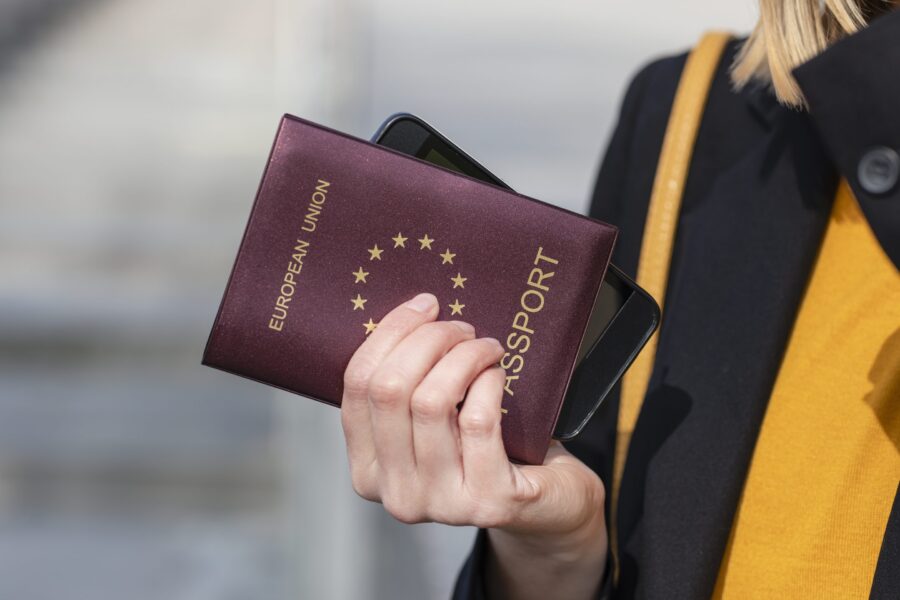 Person holding EU passport and smartphone, ready for travel in stylish attire.
