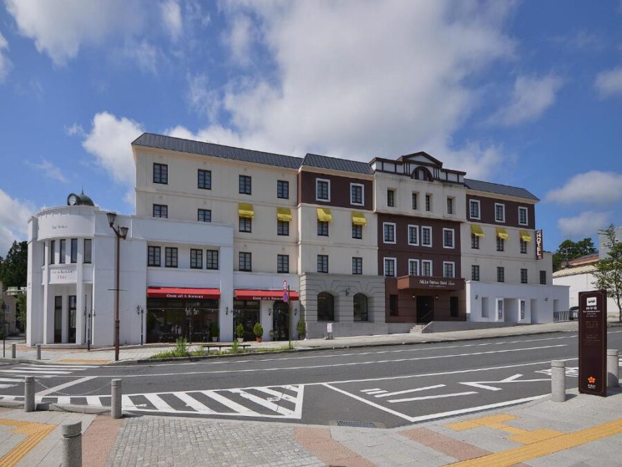 European-style city hotel exterior with shops, yellow awnings, wide street and crosswalks in Japan.