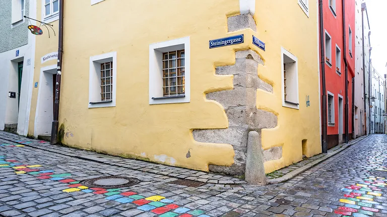 Narrow European cobblestone street corner with colorful stones and historic yellow buildings in old town.