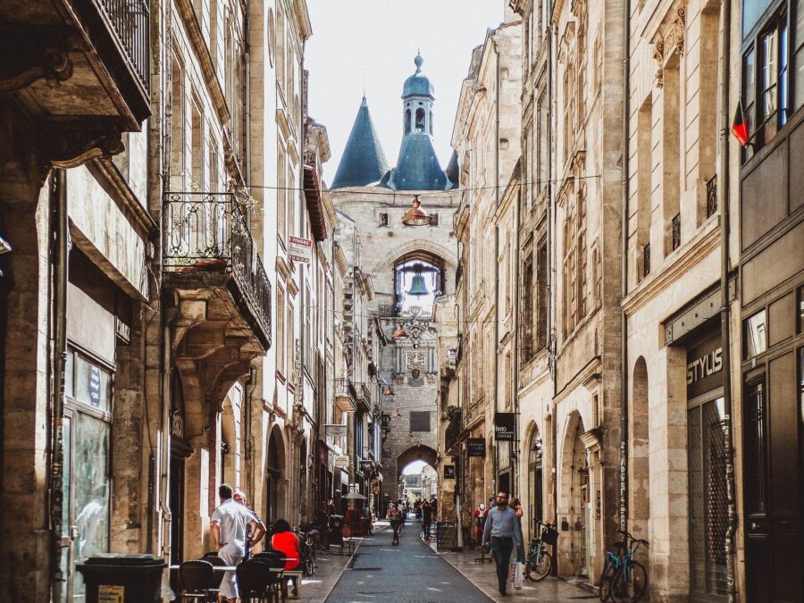 Charming European street with historical architecture, cobblestones, archway, and lively café scene.