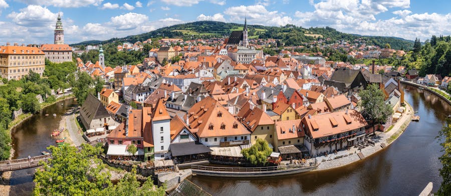 Medieval European riverside town with castle, church spire, red roofs and scenic countryside bend.