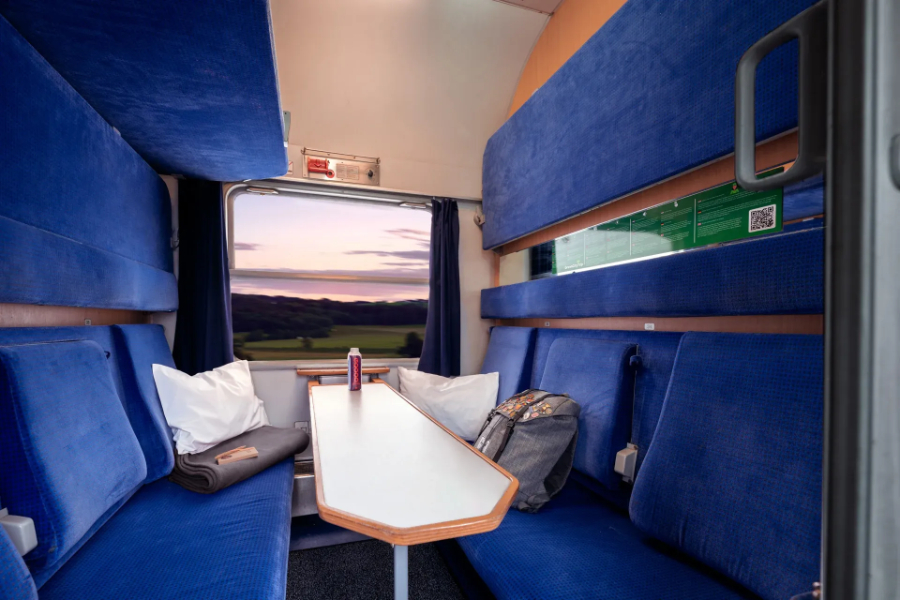 Cozy European sleeper train compartment featuring two bunk beds, a small window, and personal storage space.
