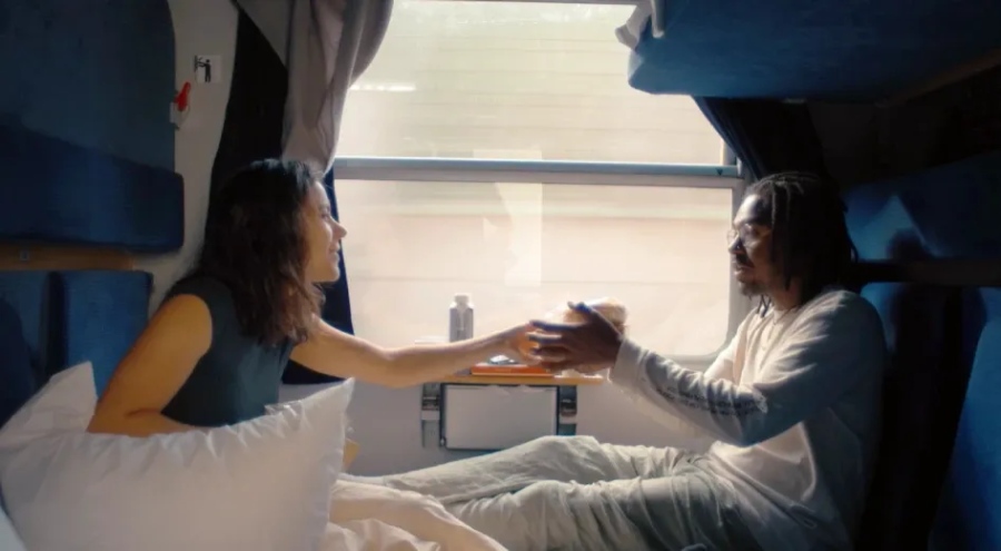Interior view of a European sleeper train compartment with bunk beds, soft lighting, and luggage storage.

