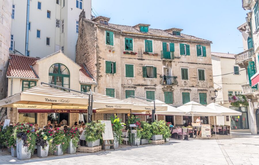 Charming European town square with Tavern Farela, outdoor dining, colorful blooms, and historic architecture.