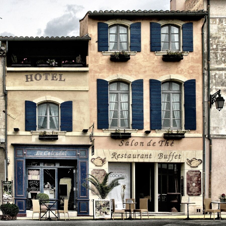 Quaint European hotel and restaurant with outdoor seating under cloudy skies.