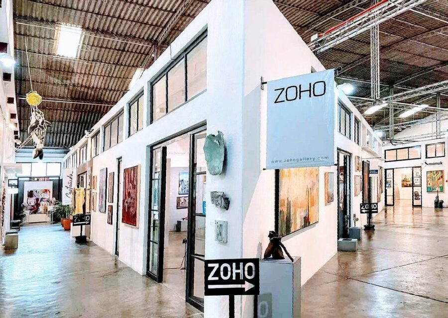 The exterior of a large white building featuring a "Zoho" sign, situated in Fabrica La Aurora, San Miguel de Allende.
