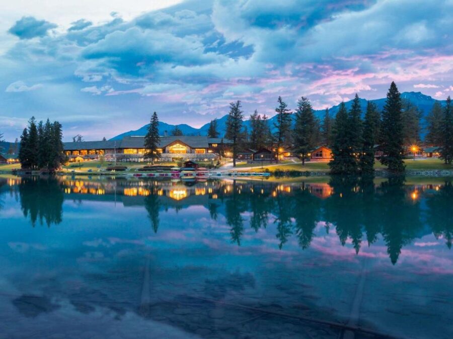 Scenic view of Fairmont Jasper Park Lodge by a lake, with majestic mountains rising in the background, Jasper, Canada.
