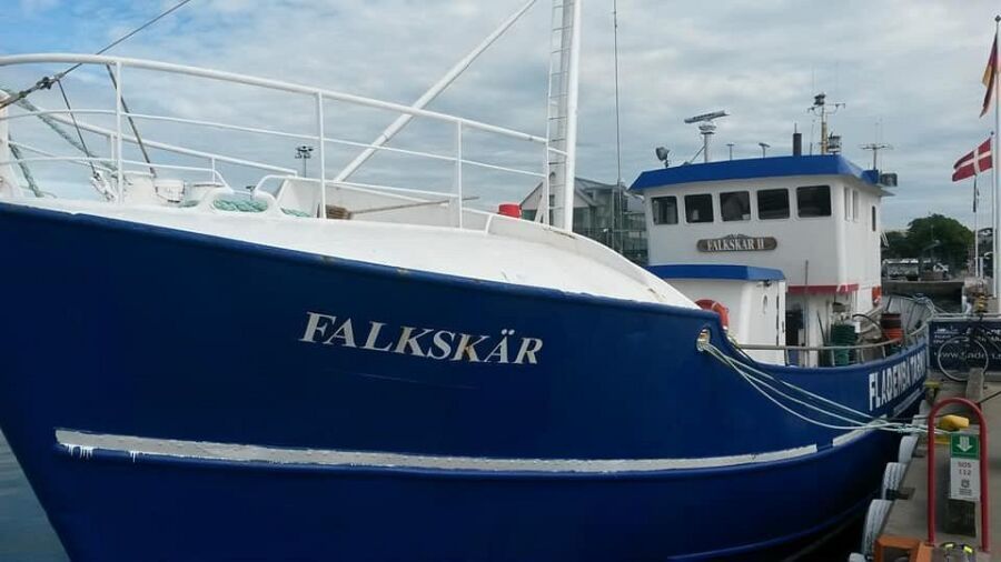 The Falkskar II, a blue and white fishing boat, is docked at a pier in Varberg, preparing for a fishing tour.
