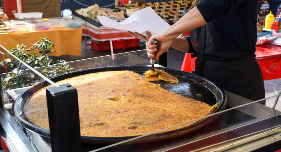 Man serves Farinata, a thin, crispy pancake from Nice, France, showcasing its soft, savory texture and golden exterior