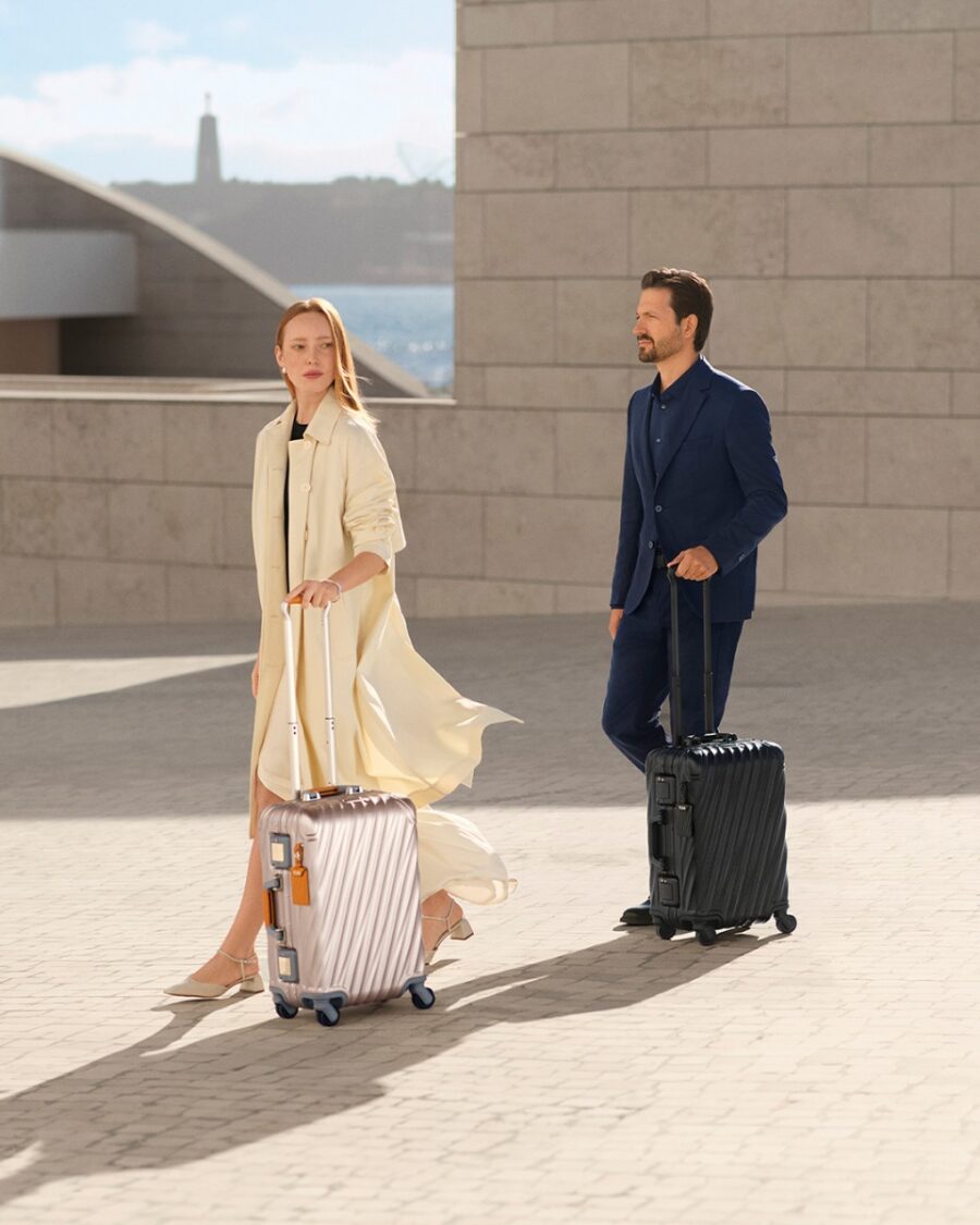 Stylish couple with suitcases walking in modern sophisticated outdoor setting.