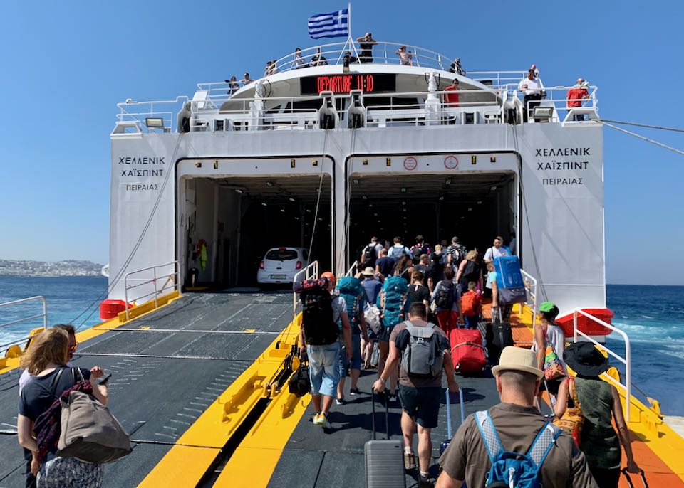 Ferry boarding scene in Greece, passengers and vehicles loading, Greek flag flying.
