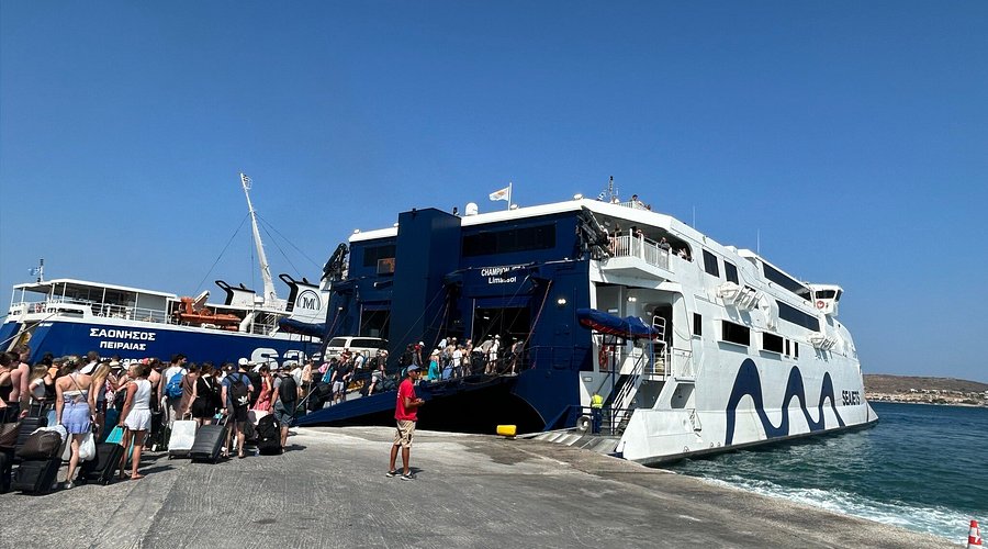 Tourists boarding Greek island ferry at sunny port pier with luggage and blue Aegean Sea.