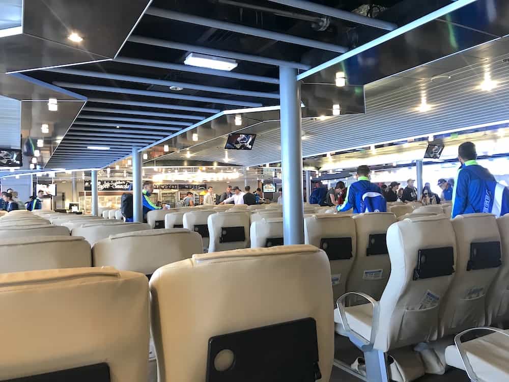 Modern ferry terminal interior with beige leather seating, passengers, and food service area.